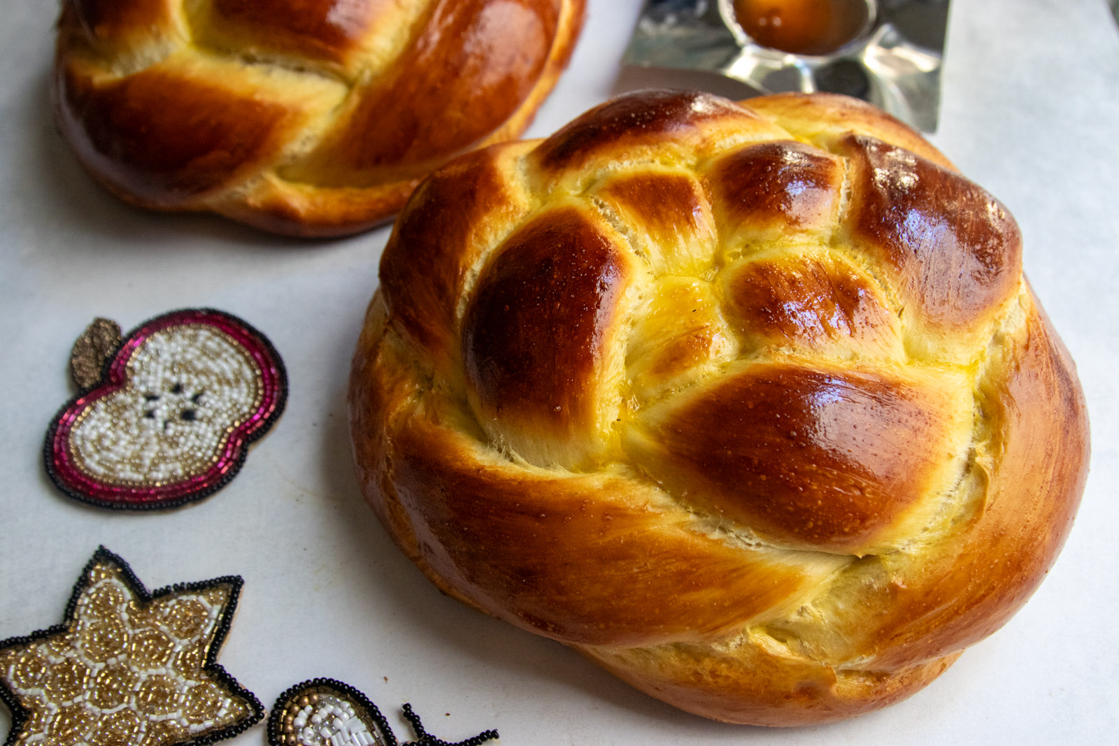 Two golden woven round challah loaves overhead with a dish of honey