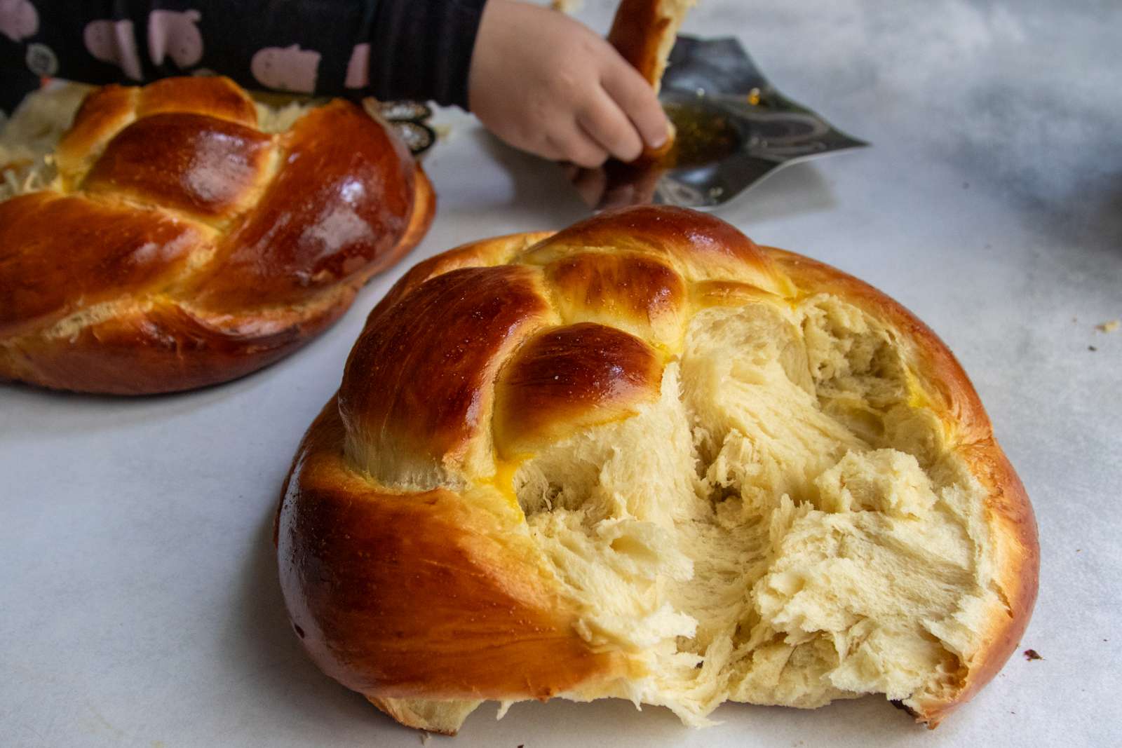 Child's hand tearing a piece from a woven round Rosh Hashanah challah