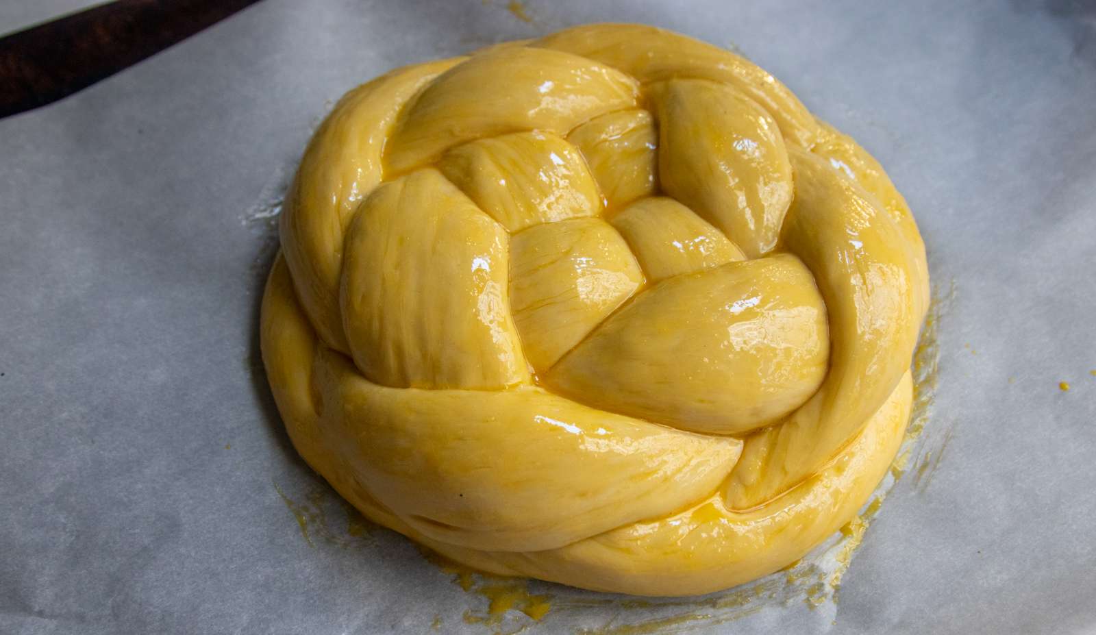 Round challah brushed with egg wash, ready to bake