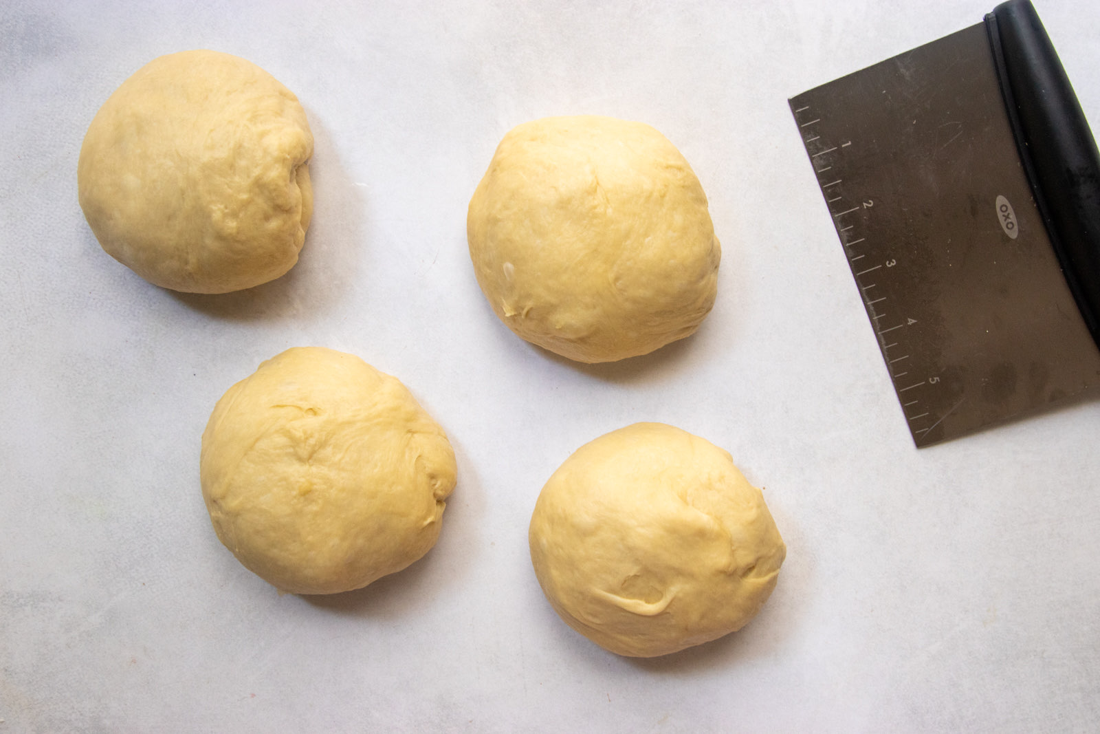 Challah dough divided into four equal balls with a bench scraper