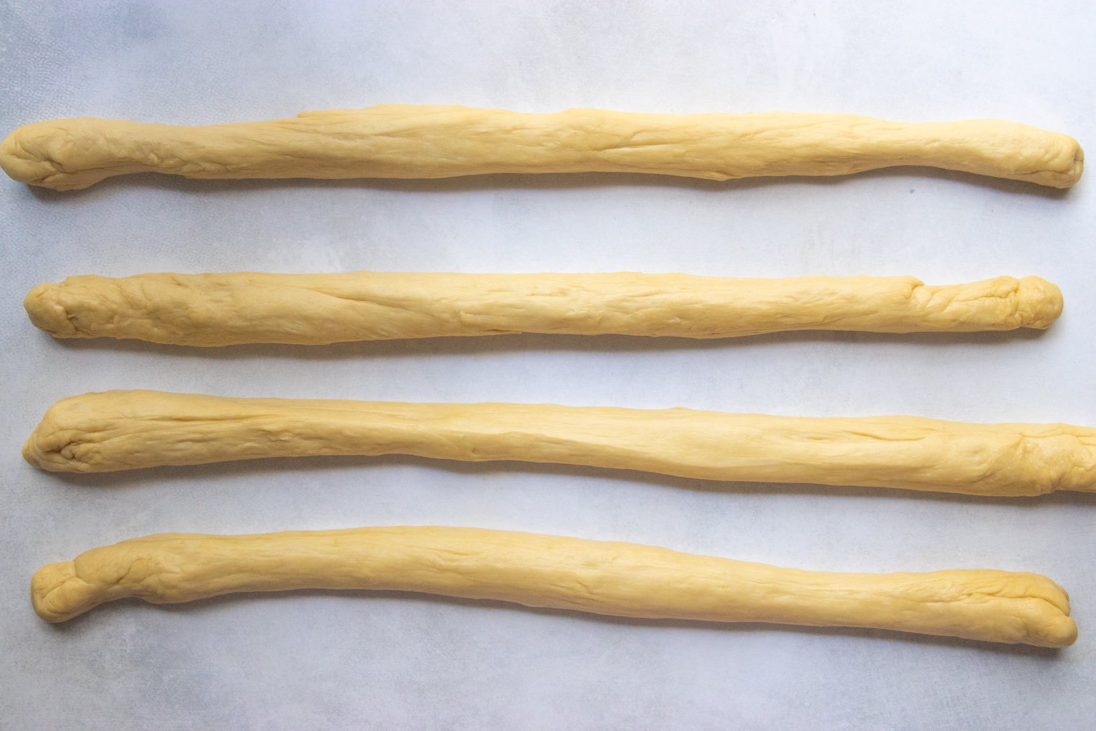 Four ropes of challah dough rolled out on parchment