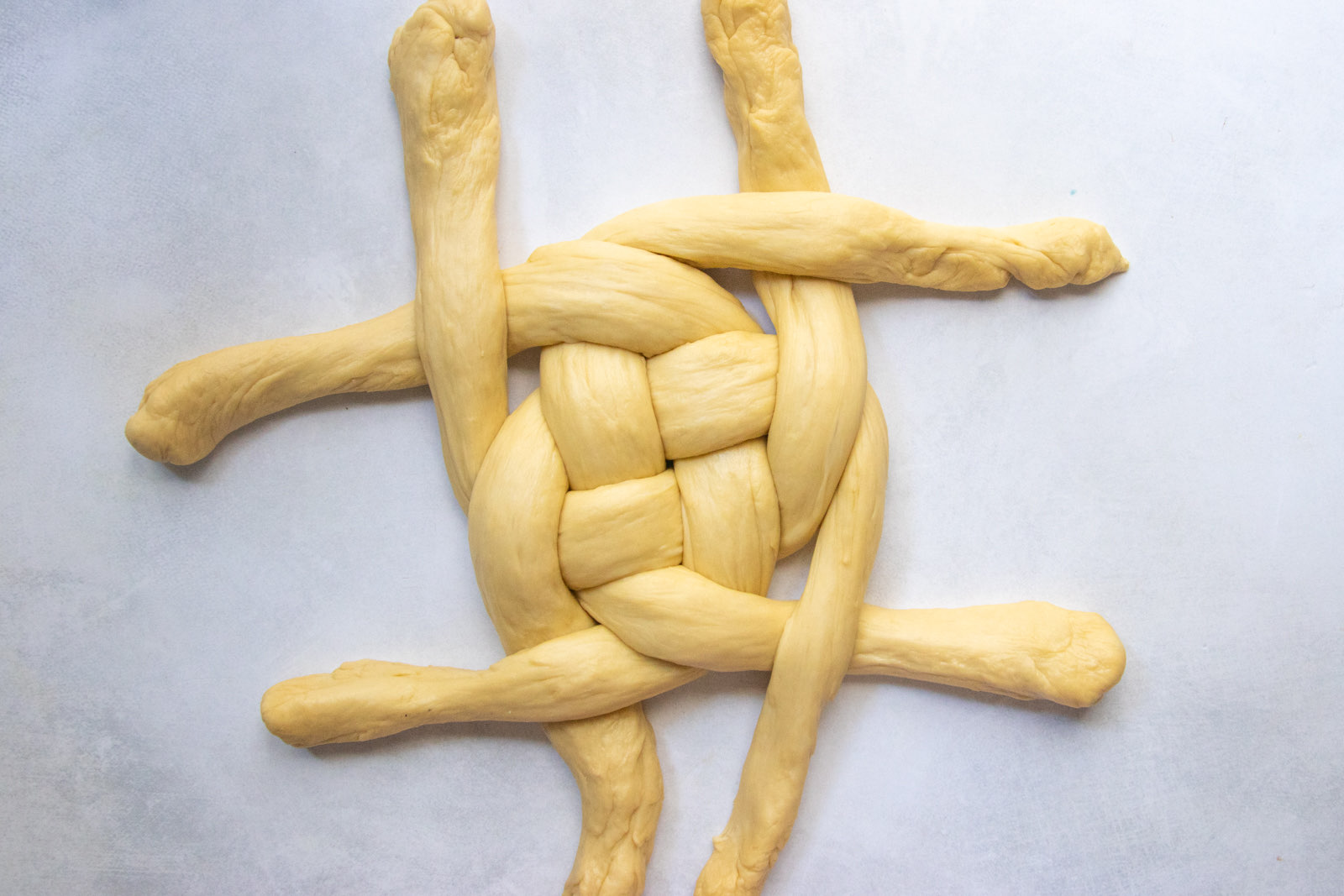 Round challah weave taking shape as the ends braid around the center