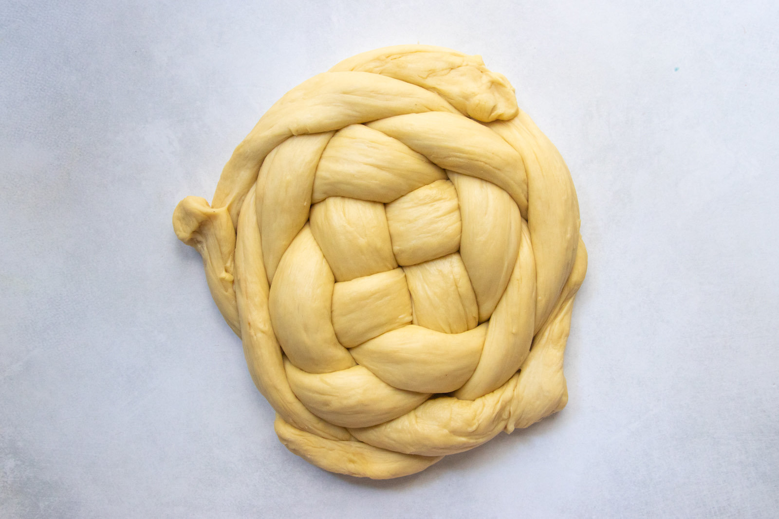 Nearly finished woven round challah with the strands braided in