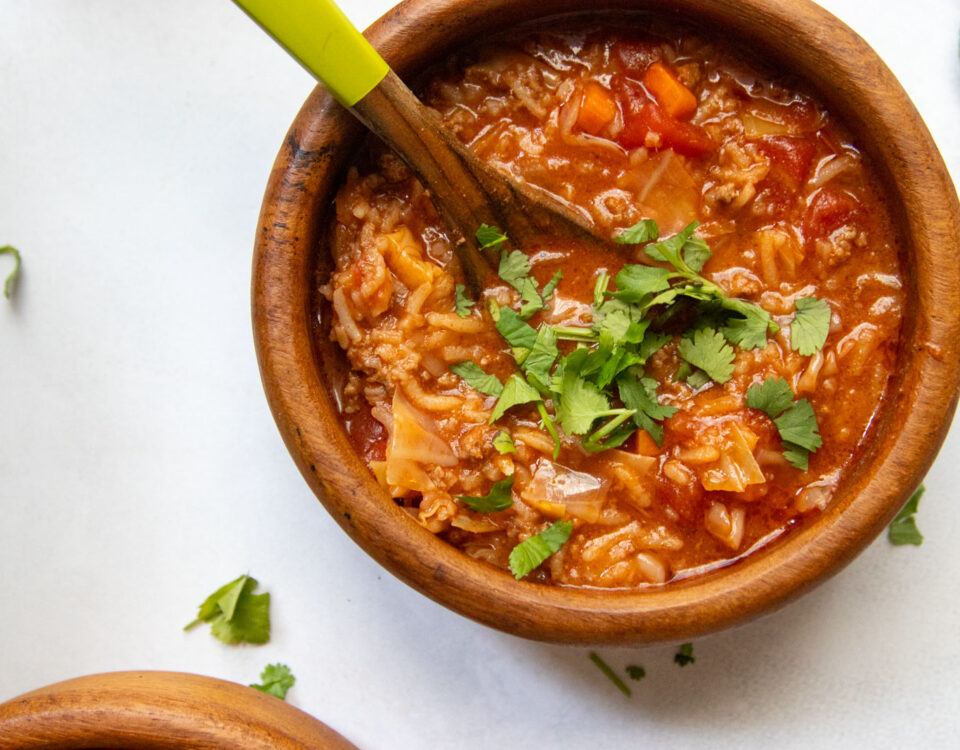 Close-up bowl of stuffed cabbage soup with ground beef, cabbage and tomatoes, topped with chopped herbs